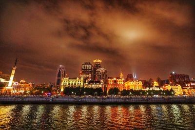Illuminated buildings by river against sky at night