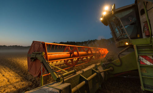 Illuminated machine harvesting crops on field at dusk