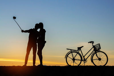 Silhouette couple taking selfie against sky during sunset