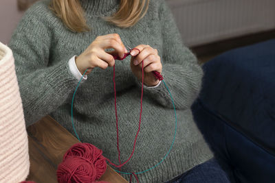 Caucasian pregnant female knits sitting in chair,woman wears warm woolen clothes