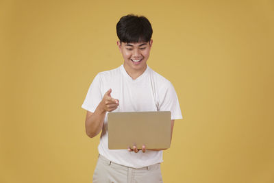 Smiling young man using smart phone against yellow background