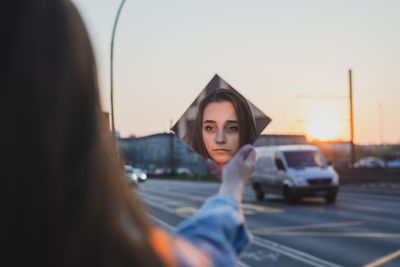 Woman holding mirror against sky during sunset