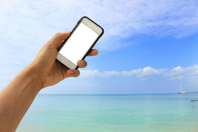 Close-up of hand holding smart phone against sky