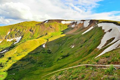 Scenic view of green mountain against cloudy sky