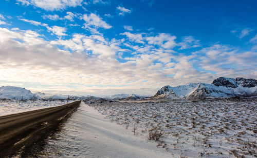 Road by snowcapped mountains against sky during winter