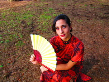 High angle portrait of woman holding red leaf outdoors