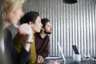 Creative business colleagues sitting at conference table while looking away in board room