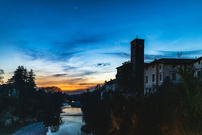 Silhouette buildings by trees against sky at sunset