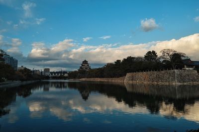 Okayama castle with reflection in asahi river against sky