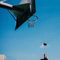 Low angle view of people playing basketball against blue sky