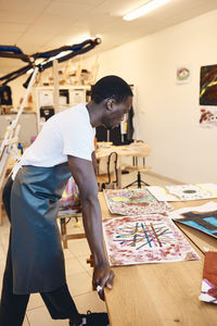 Side view of young man looking at painting on table in art class