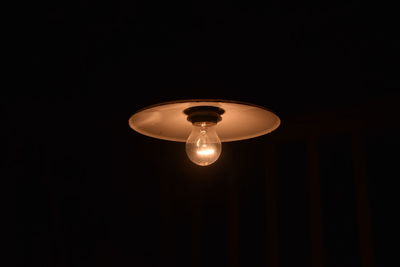 Low angle view of illuminated light bulb hanging from ceiling