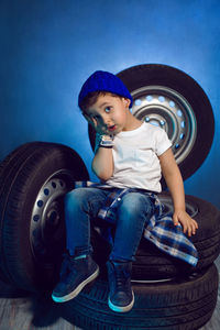 Boy in a white t shirt shirt and hat sits on a background of car wheels on a blue