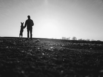 Silhouette men standing on field against clear sky, mans best friend