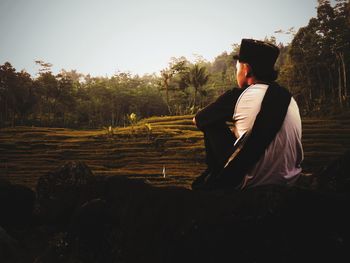 Rear view of man sitting on field against sky