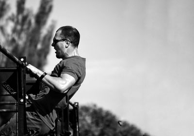 Side view of young man standing by railing against sky