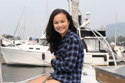 Portrait of smiling young woman sitting on boat against sky