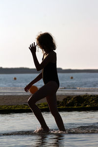 Girl wading in sea against clear sky during sunset