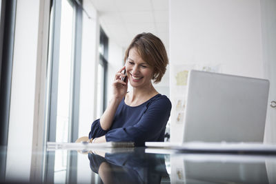 Smiling businesswoman on cell phone at office desk