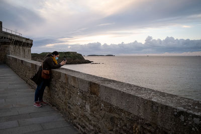 Man walking on retaining wall by sea against sky