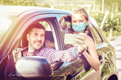 Young couples on road trip taking selfie with face mask while driving on countryside