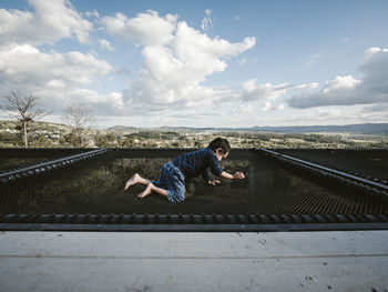 Side view of boy crawling on netting against sky