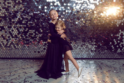 Two sisters in black long dresses stand in the studio against the lights