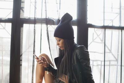 Young woman using phone while standing on window
