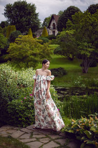 Outdoor portrait of a beautiful luxury brunette woman in a dress with flowers stands