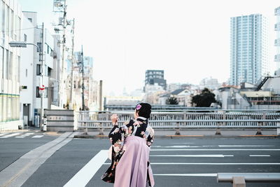 Rear view of people on road in city against clear sky