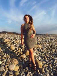 Full length of woman standing on rock at beach against sky