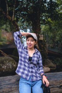 Portrait of young woman standing against trees