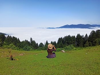 Rear view of woman sitting on field against sky