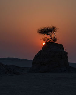 Silhouette rock formation on shore against sky during sunset