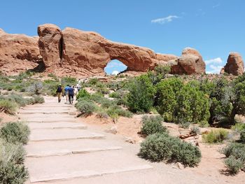 Mid distance view of people walking against rock formations during sunny day