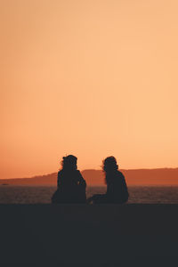 Rear view of silhouette people at beach against sky during sunset