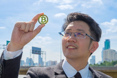 Portrait of young man holding eyeglasses against sky