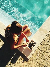 High angle view of young woman eating fruits while sitting at poolside