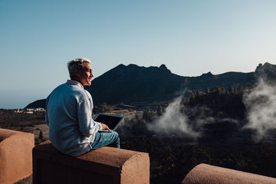 Man sitting on mountain against clear sky