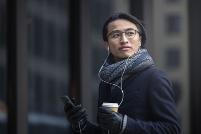 Handsome man with smartphone and paper cup on street