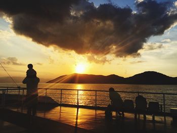 Silhouette people on promenade by sea against sky during sunset