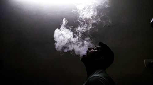 Portrait of young man smoking against black background