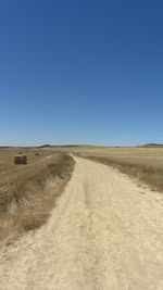 Road amidst field against clear blue sky