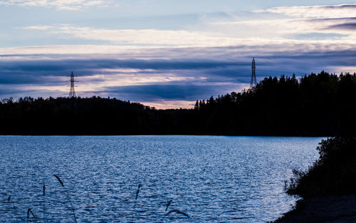 Silhouette trees by calm lake against sky