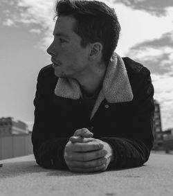 Close-up of young man lying on retaining wall against sky