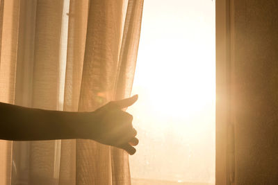 Cropped hand holding curtain on window