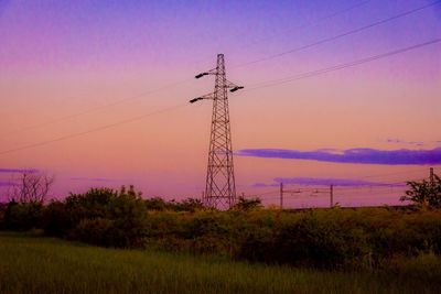 Low angle view of electricity pylon on field against sky at sunset