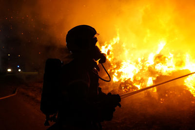 Silhouette firefighter extinguishing fire at night