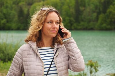Young woman using phone while standing against trees