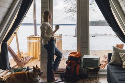 Woman enjoying drink leaning by glass door at home